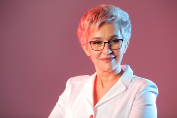 beautiful stylish woman aged, wearing glasses, in a white jacket on a pink background