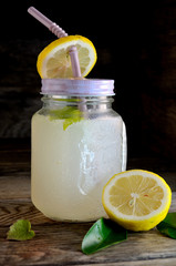 Homemade lemonade with mint and lemon on a wooden table in a glass with a straw.