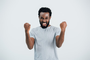 excited african american man in grey t-shirt posing isolated on grey