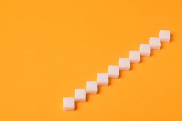 Ladder from sugar cubes over orange background