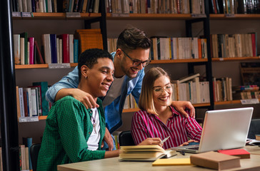 Three young students study in the school library and using laptop for researching online.