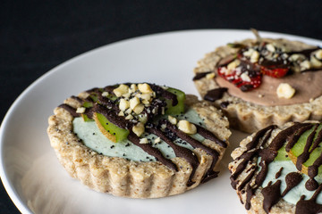 Raw vegan tartlets on the white plate. Healthy desserts, close up