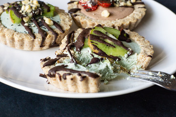Raw vegan tartlets on the white plate. Healthy desserts, close up