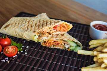 shawarma and french fries with sauce lies on a dark bamboo background. Eastern fast food. Beautiful...