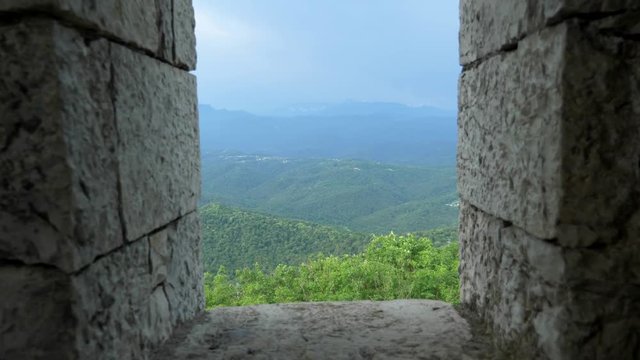 stone wall and arched window openings with a view of a mountain range with forest and haze over the mountains