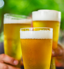 Close-up view of a three glass of beer in hand. Beer glasses clinking at outdoor bar or pub