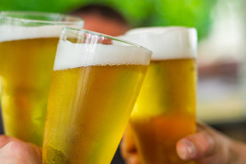 Close-up view of a three glass of beer in hand. Beer glasses clinking at outdoor bar or pub