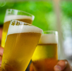 Close-up view of a three glass of beer in hand. Beer glasses clinking at outdoor bar or pub