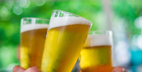 Close-up view of a three glass of beer in hand. Beer glasses clinking at outdoor bar or pub