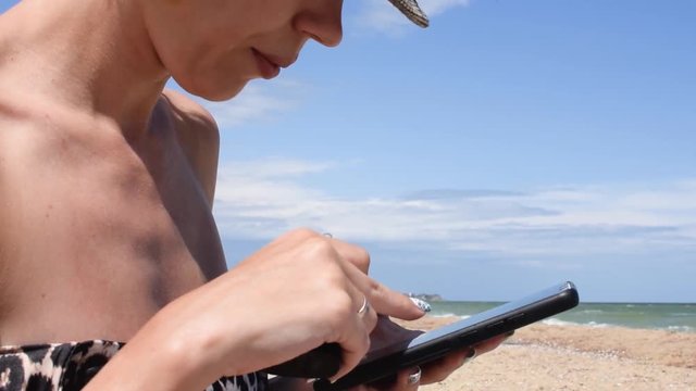 A Woman Of Middle Age In A Bathing Suit Writes The Text In The Phone And Smokes On The Seashore, The Ocean.