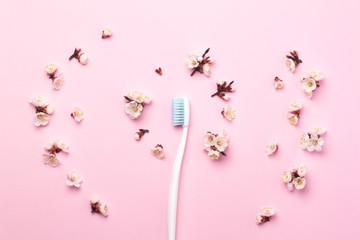 White toothbrush with blue bristles on a pink paper background decorated with spring flowers.