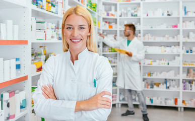 Portrait of a female pharmacist, male colleague working with drugs in the background.
