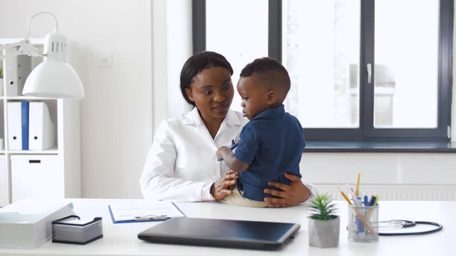 medicine, healtcare and pediatry concept - happy african american female doctor or pediatrician holding baby boy patient on medical exam at clinic