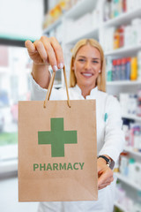 Pharmacist holding paper bag with a green Pharmacy logo in a drugstore