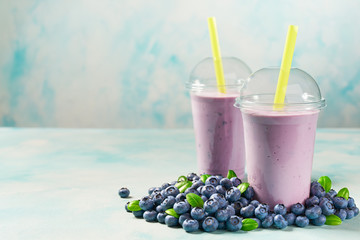 Freshly blended fruit smoothie with blueberry  in plastic cups on a turquoise  background, with...