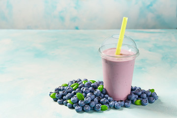 Freshly blended fruit smoothie with blueberry  in plastic cups on a turquoise  background, with...