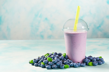 Freshly blended fruit smoothie with blueberry  in plastic cups on a turquoise  background, with...