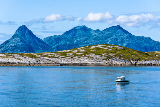 Rocks of Landegode island as seen behind Hjartoya Island in Bodo Municipality, Nordland county of Norway. Water of Norwegian Sea and small boat are at foreground.