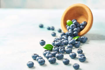 Fresh blueberries are scattered from a wooden bowl on a turquoise background, selective focus.