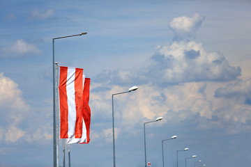Flaga na maszcie i latarnie uliczne na tle zachmurzonego nieba. 