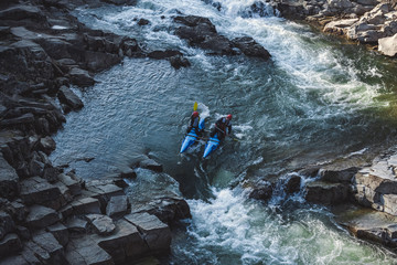 Two man on whitewater catamaran are going through the rapid on the mountain river in early spring