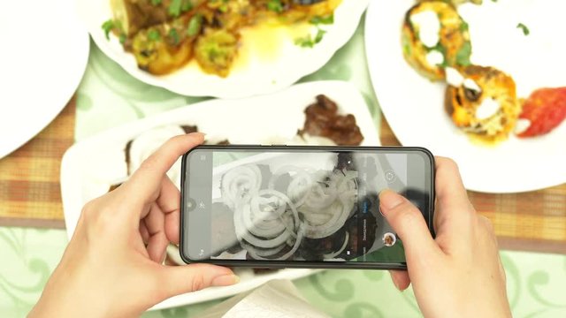 Female hands make photo on a smartphone in a restaurant with dishes of Caucasian cuisine. grilled vegetables, shashlik, sauce