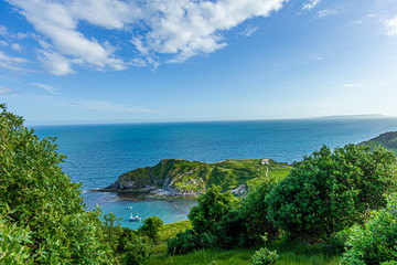 A view of the Lulworth Cove along the Jurrassic Coast in Dorset under a majestic blue sky and some white clouds.