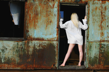 Blonde wooman with long hair and white shirt posing in old metal building