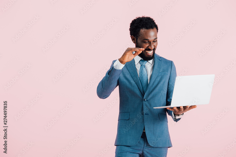 Wall mural happy african american businessman having video chat on laptop isolated on pink