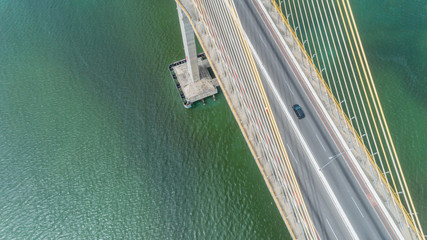 Aerial view of car driving on a bridge with natural forest trees, sand, tropical beach and waves rolling into the shore.