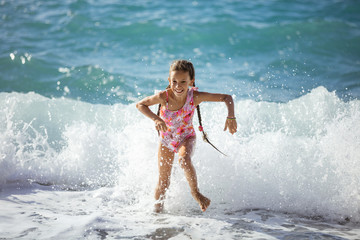 Happy young girl playing on beach and running away from big waves