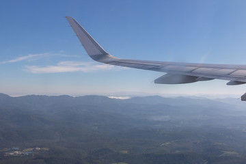 Wing of plane with beautiful sunrise skyline. Airplane flying on blue sky. View from airplane window. Commercial airline flight in the morning with sunlight. Plane wing above clouds.