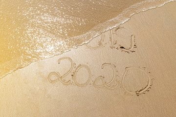 Happy new year. 2020 and 2019 written on the sand where 2019 is getting washed away by the wave