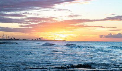 Scenic sunset over the sea. The sun sets on the water. Clouded sky is painted with bright colors. Sunset beach in a summer evening. Brazil.