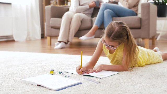 education, family and three generations concept - student girl with notebook lying on floor at home and doing homework
