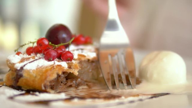 close-up. Apple strudel with vanilla ice cream. Hands cut a piece of cake with a fork and knife