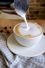 Closeup image of male hands pouring milk and preparing fresh cappuccino, coffee artist and preparation concept, morning coffee