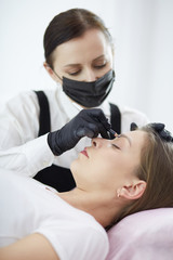 Cosmetologist applying permanent make up on eyebrows