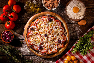Pizza tuna fish, onion, tomato and black olive on wood background. Top view, close up. Traditional Brazilian Pizza.