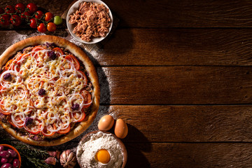 Pizza tuna fish, onion, tomato and black olive on wood background. Top view, close up. Traditional Brazilian Pizza.