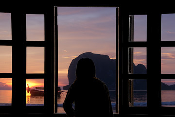The silhouette of a young woman looking sunset the window with sea views.
