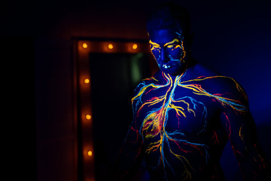 UV Patterns Body Art Of The Circulatory System On A Man's Body. On The Torso Of A Muscular Athlete, Veins And Arteries Are Drawn With Fluorescent Dyes. Bodybuilder Standing By The Mirror With Lamps.