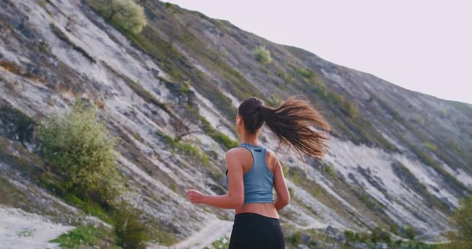 Sporty young woman doing her workout in the middle of mountain she running hard through the stones road , amazing landscape view