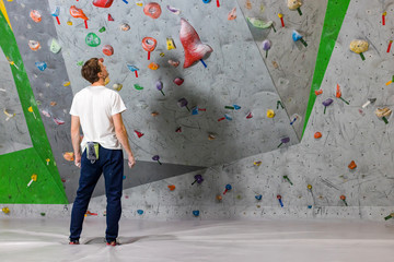 Rock climber stands and looks at the climbing wall with hooks in the boulder hall