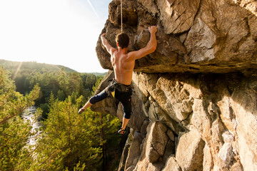 Climber Extreme climbs a rock on a rope with the top insurance, overlooking the forest