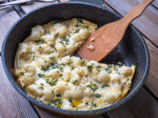 Cauliflower fried in eggs on a round cast iron skillet