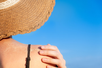 Summer holidays mood: female shoulder covered in sand in bright blue background. Back of a young...