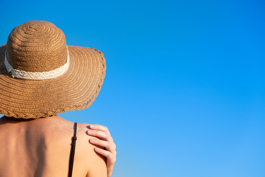 Summer holidays mood: female in beach hat, covered in sand in bright blue background. Shoulders of a young woman in a retro hat, chot from behind