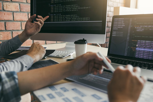 Two software developers are using computers to work together with their partner at the office desk.