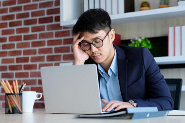 Tired asian man sleeping at office desk. Young businessman with eyeglasses overworked and fell asleep, Office man take a nap at his working place